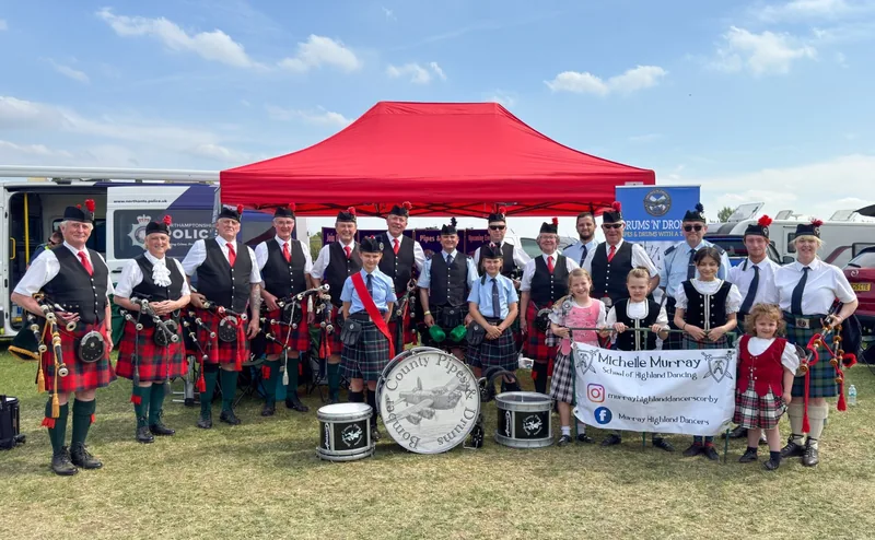 The band and young dancers lined up in front of a red gazebo at a summer show